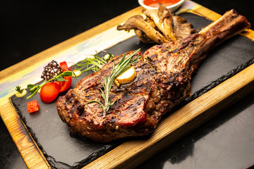 Grilled Tomahawk steak ribeye with rosemary, butter and cherry tomatoes on wooden plate