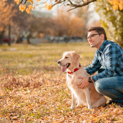 Young man hugging golden retriever dog in autumn outdoors