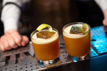 Two cocktails with lemon and lime peel on the bar