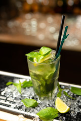 Mojito cocktail with lime and mint on the bar, crushed ice, blurred background.