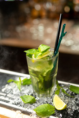 Mojito cocktail with lime and mint on the bar, crushed ice, blurred background.