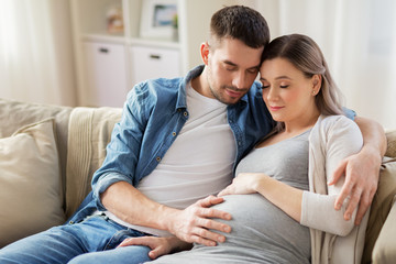 pregnancy and people concept - happy man hugging pregnant woman at home - obrazy, fototapety, plakaty