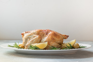 Roasted chicken with potatoes and rosemary on white table. Copy space.