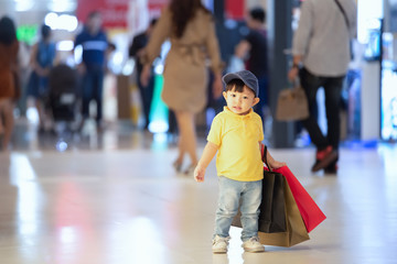 Kid shopping. Asian little boy in yellow shirt and jeans enjoyment of shop. Walk in the shopping mall and holding heavy shopping paper bags.
