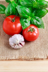 Tomatoes, garlic and basil plant on jute sack background.