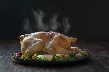 Roasted hot chicken with potatoes and rosemary on wooden black table. Copy space.
