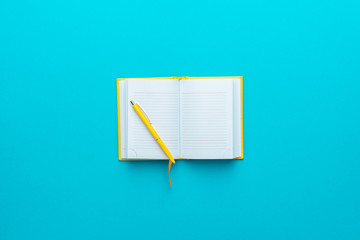 Top view of opened notebook and yellow pen over it in the centre of turquoise blue background with...