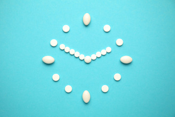 White medical pills in shape of clock on blue background. Health care, vitamins for elderly.