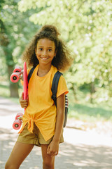 African American schoolgirl smiling at camera while holding skateboard