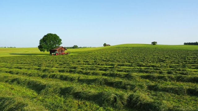 Old Fendt tractor with trailed rotary tedder. Hay ready to be harvested. Wood storage in the countryside for tools. Hilly environment in Germany