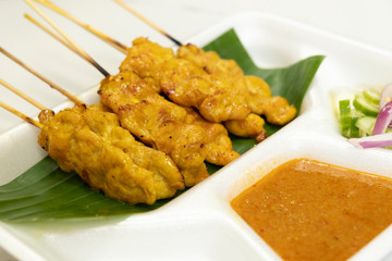 Close-up grilled pork satay with peanut sauce and pickles which are cucumber slices and onions in vinegar on white plate, asian food style and thai street food style.