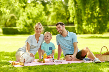 family, leisure and people concept - happy mother, father and little son having picnic at summer park