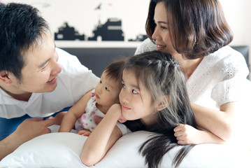 Obraz na płótnie Canvas Happy family activity portrait concept. Asian mother and little two daughters looking at father with smile. They all are lying on the bed in the morning feeling happy spending time together.