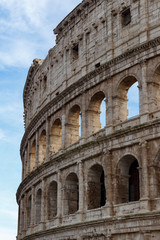 Obraz premium Detail of the Colosseum, under a blue sky with white clouds.
