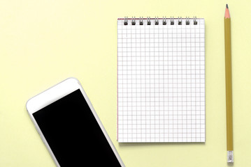Blank notepad, phone and pencil on yellow background close up