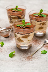 Classic tiramisu dessert in a glass cup and strainer with cocoa powder on concrete background