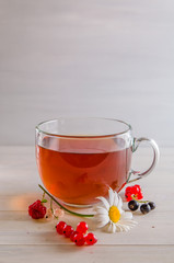 tea in a mug with berries and chamomile on a white background