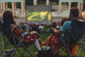 couple sitting in camp-chairs in city park looking movie outdoors at open air cinema