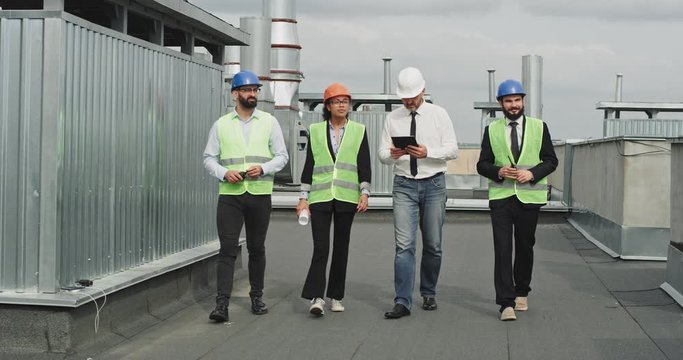 Charismatic multi ethnic people two businessman engineer and architect analyzing and discuss the plan of construction site they wearing a safety helmets