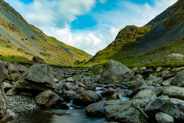 Long exposure photo of a stream next to a mountain serpentine road with nicely blurred water and clouds and sharp mountain slopes - Lake District, United Kingdom