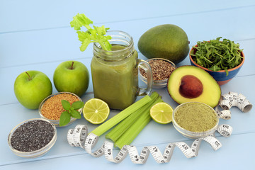 Health food diet drink with fresh fruit, vegetables, matcha powder, flax, chia and hemp  seed on blue wood background with tape measure. High in omega 3, antioxidants, vitamins and dietary fibre.