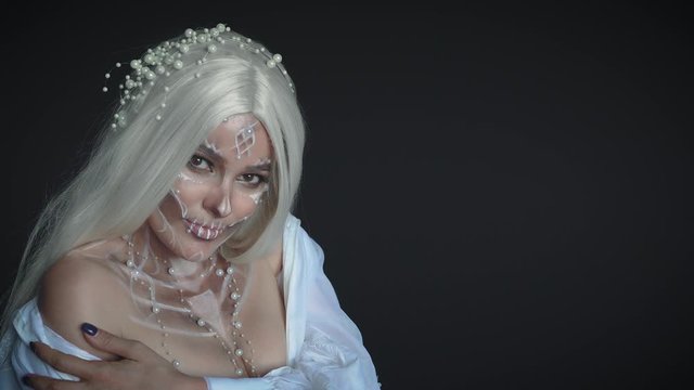 seductive beauty of death goddess, corpse of bride rose from the dead and beckons into dark room. woman with sweet skull mask shows bare shoulder, charming embarrassed girl with pearl jewelry