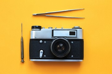 Vintage camera lens and tools, tweezers and a screwdriver with yellow paper background, camera repair concept.