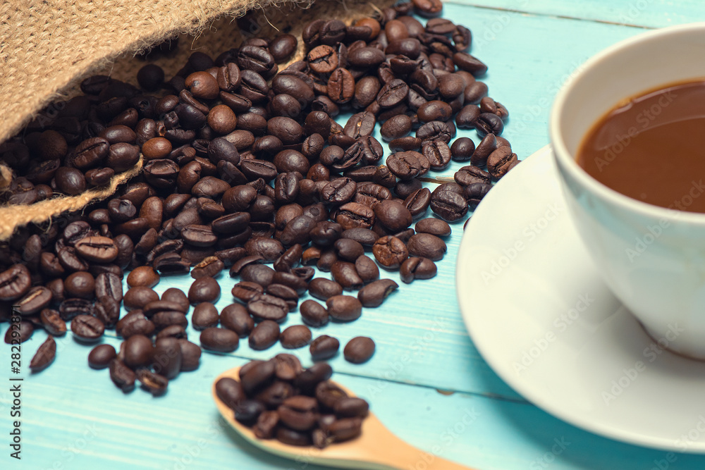 Wall mural cup of hot coffee and roasted coffee beans from the sack bag on a wooden table and spoon at the back