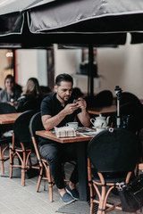 Stylish young man in an Italian cafe on the terrace in the city uses a smartphone