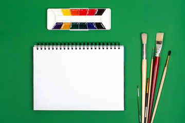 White notebook with paints and brushes for drawing. The photograph on the subject of creativity.