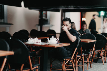 Stylish young brunette man sits in a cafe on the terrace and drinks coffee. Italian street