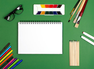 White notebook with paints and brushes for drawing. The photograph on the subject of creativity.