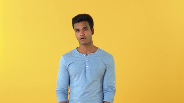 Clueless puzzled young Indian man shrugging his shoulders expressing uncertainty on yellow background 