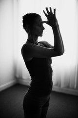 Classical black and white art photography of a woman practicing advanced yoga pose indoors on a...