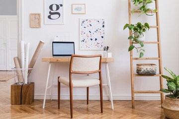 Design scandinavian interior of home office space with stylish chair, wooden desk, ladder, laptop, commode, elegant accessories and mock up posters frames. Stylish home decor. Template. White wall. 
