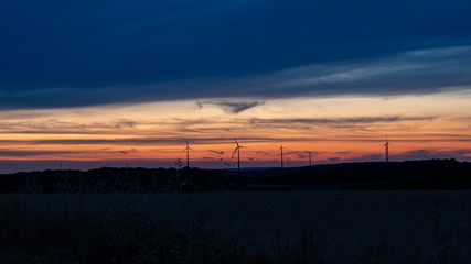 Fototapeta na wymiar Cloudy sunset sky with silhouettes of wind turbines. 