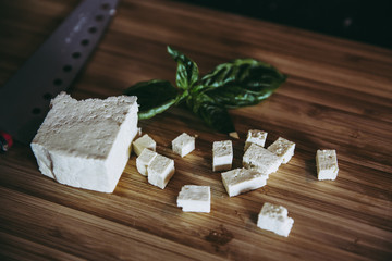 Cuts of fresh tofu small pieces with green basil on wooden kitchen board. home vegan food