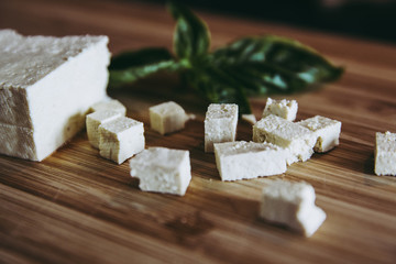 Cuts of fresh tofu small pieces with green basil on wooden kitchen board. home vegan food