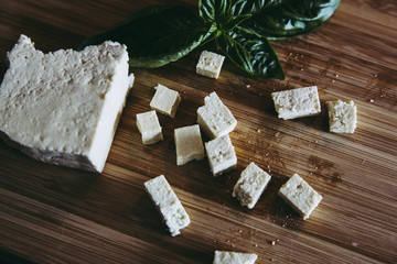 Cuts of fresh tofu small pieces with green basil on wooden kitchen board. home vegan food