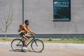 stylish african american businessman riding bicycle on sunny street