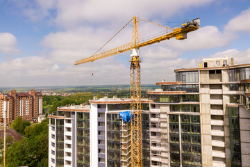 Naklejka premium Apartment or office tall building under construction. Brick walls, glass windows, scaffolding and concrete support pillars. Tower crane on bright blue sky copy space background.