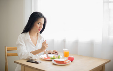 Obraz na płótnie Canvas Asian women in white shirt holding a knife on the plate of breakfast, Looking at the camera with a fierce face, The importance of breakfast concept-Image