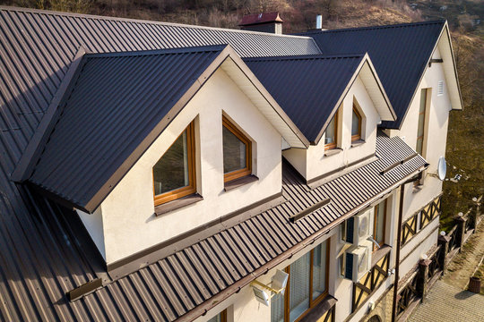 Close-up aerial view of building attic rooms exterior on metal shingle roof, stucco walls and plastic windows.