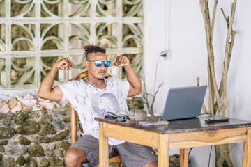 Portrait of Cheerful african american man in a sunglasses, works on laptop and showing off his muscles.