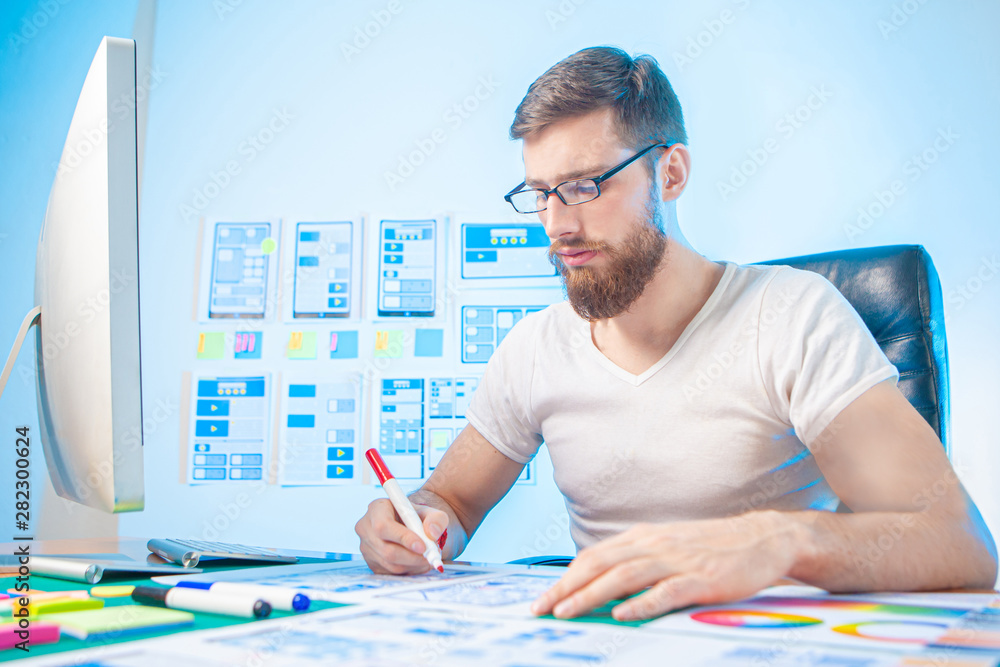 Poster a man works at a computer. designer near the computer. man is working on application design. office 