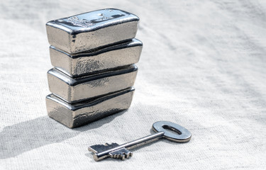 Silver bars and the key to the safe against a rough texture of the light coloured fabric.