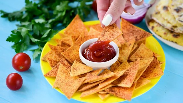 Woman hand dip corn tortilla mexican nacho chip into tomato sauce. Tex mex food. Real time footage