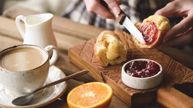 Person spread jam on sweet bun for breakfast. Tasty cozy comfortable breakfast in cafe with croissant, coffee, orange and jam