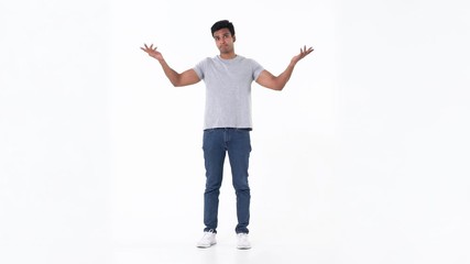Portrait of puzzled and confused handsome young Indian man in plain blue jeans and grey t-shirt shrugging his shoulder on white background - Powered by Adobe