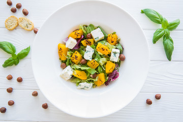 Pumpkin salad with cheese, croutons, hazelnut and basil leaves. Autumn food on white wooden rustic table. Top view. 